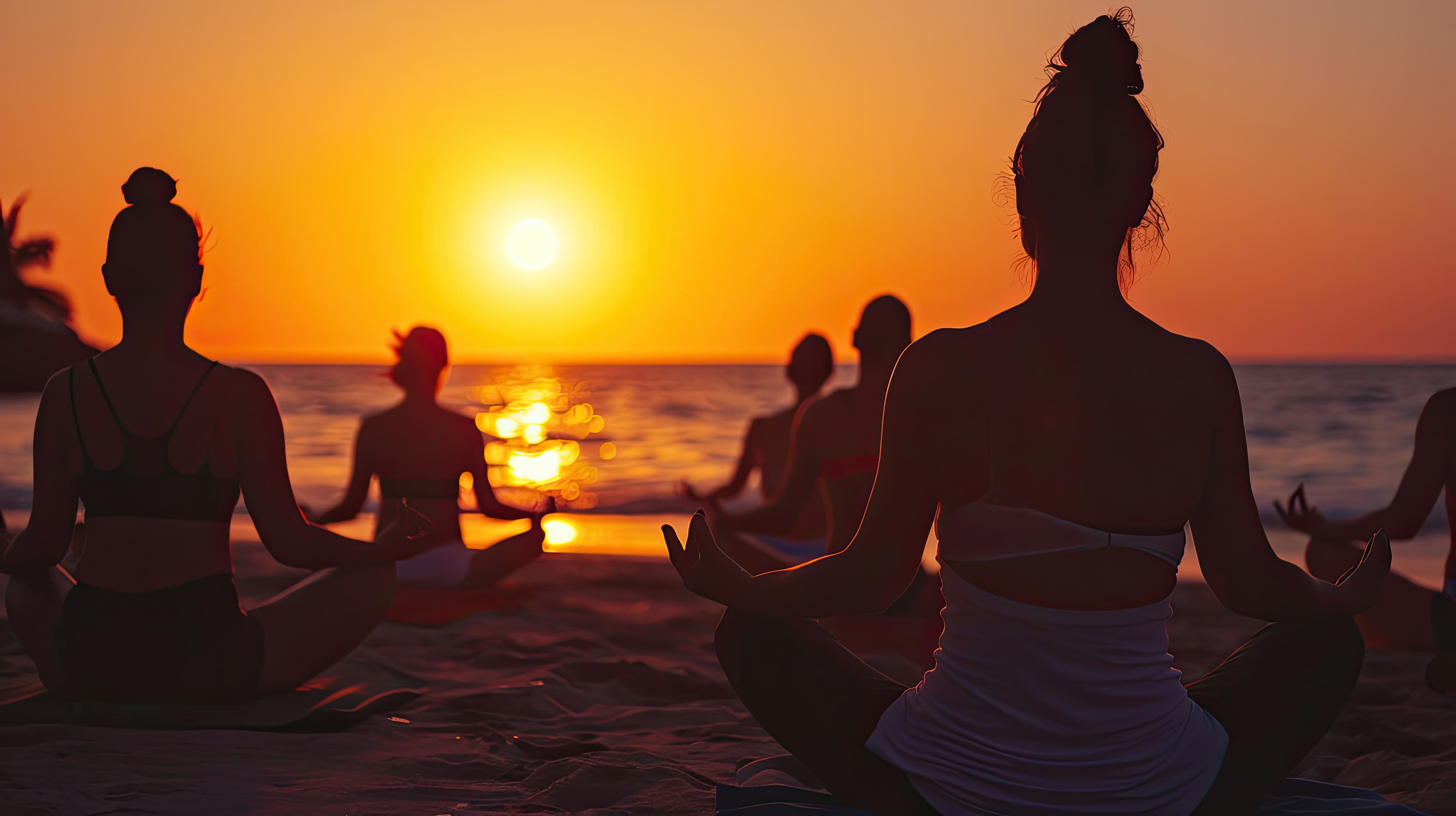 A group meditating on the beach at sunset